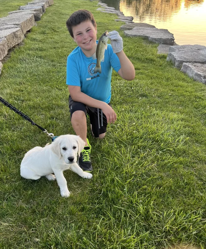 Kid Captain Cooper Estenson holding a fish while a dog lays beside him