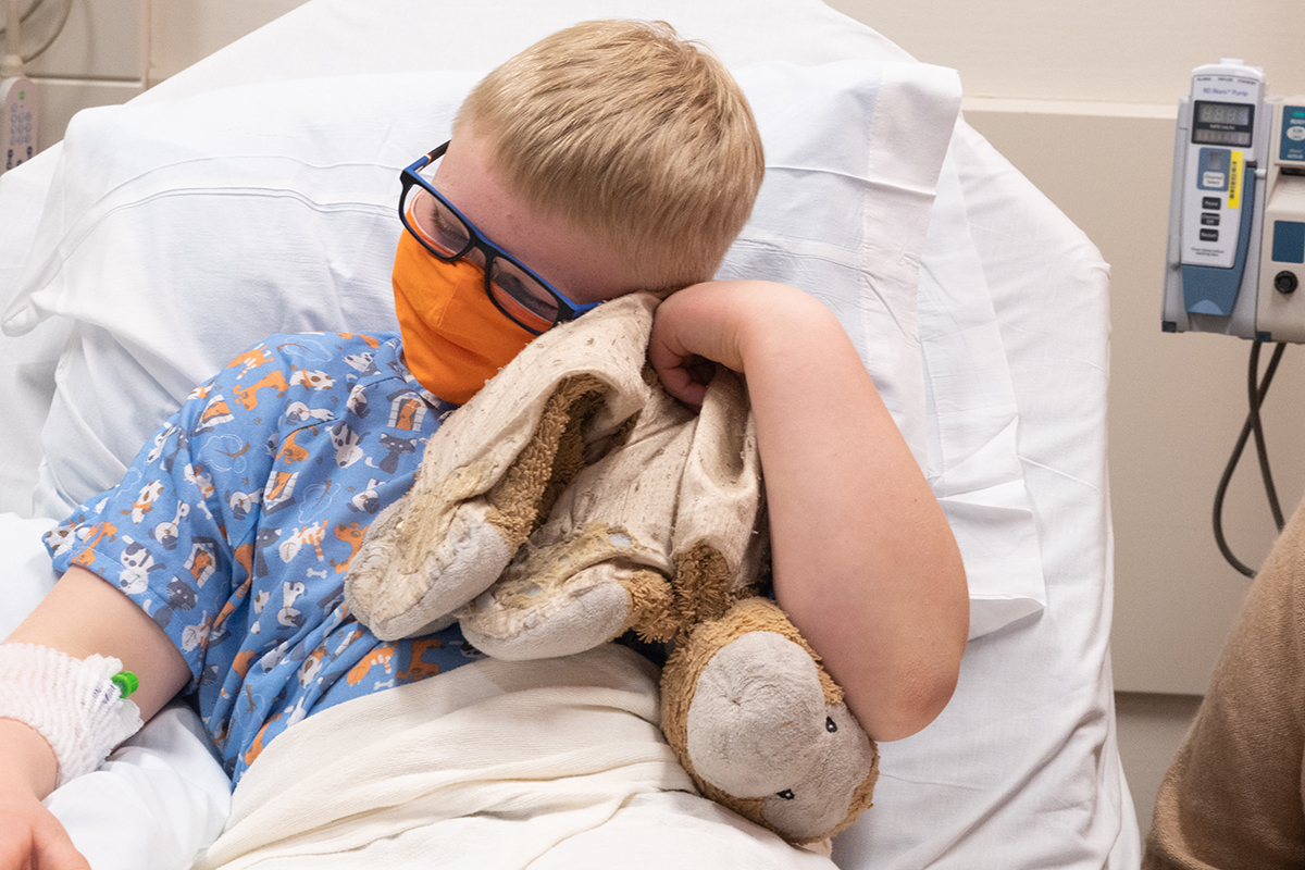 Child holds their stuffed animal while laying in a hospital bed