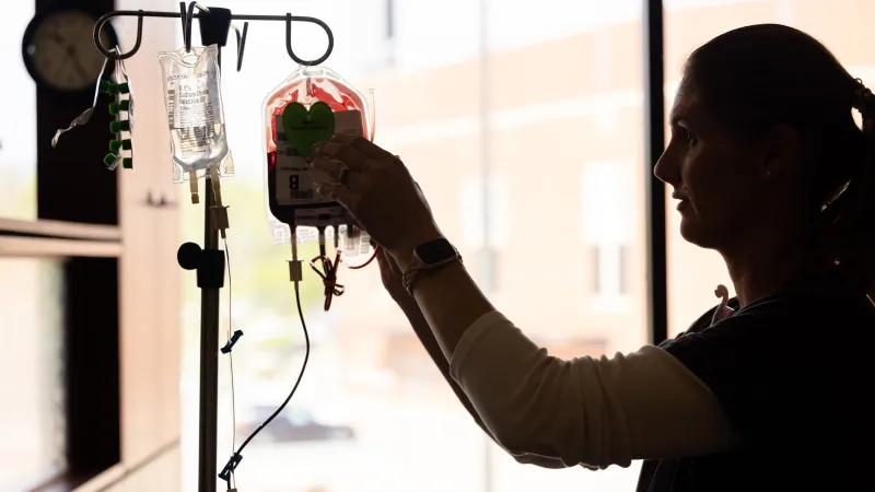 A nurse hangs an infusion bag on an IV pole.