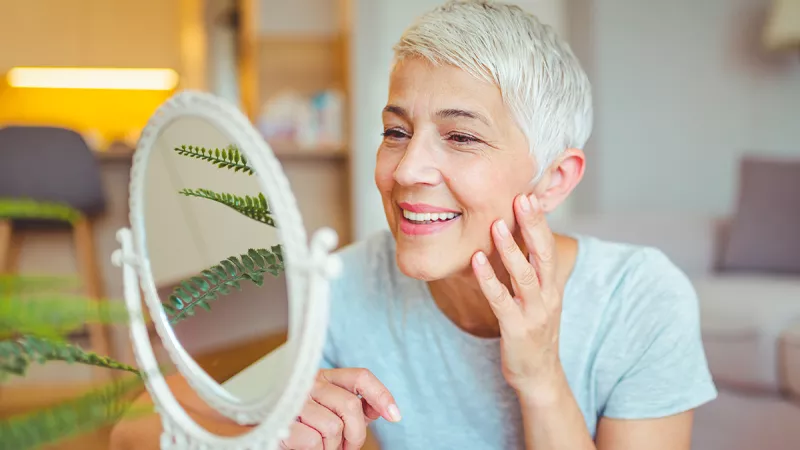 Woman smiling as she looks at her face in a mirror