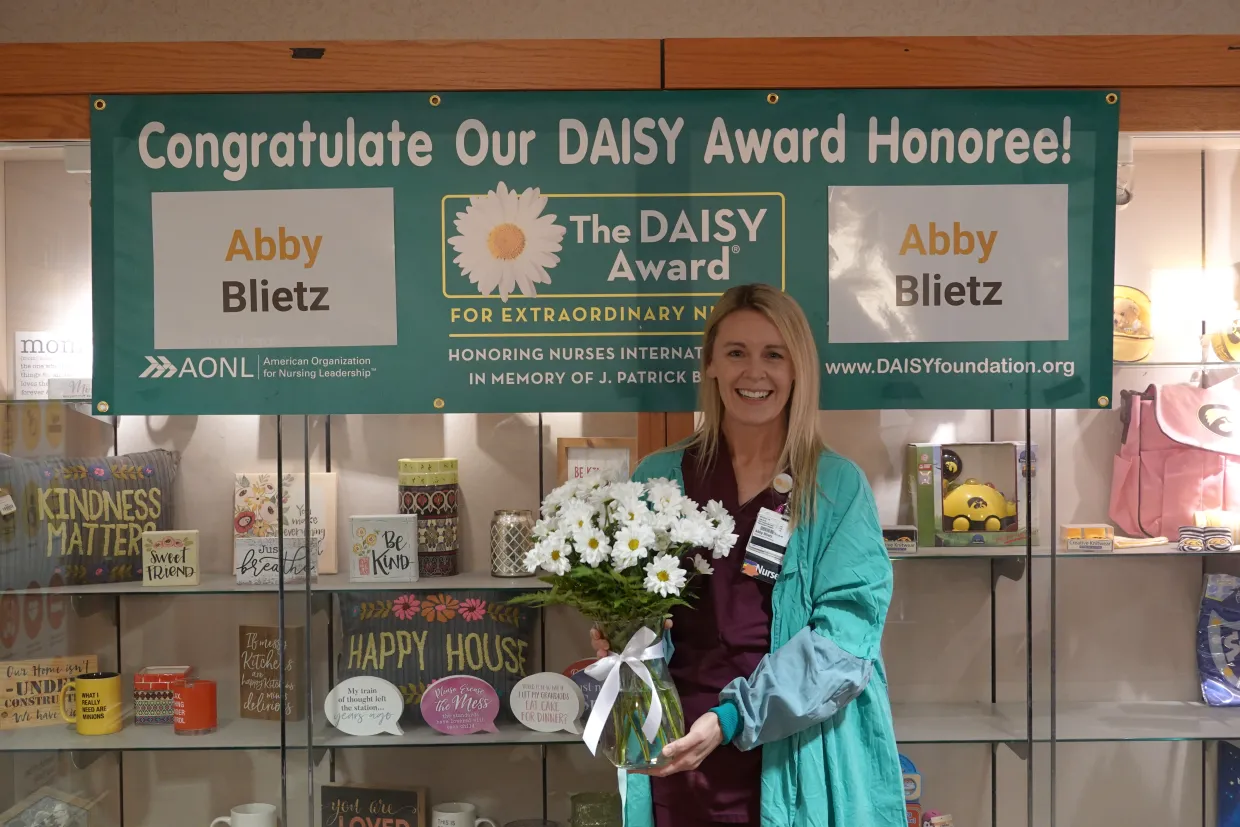 Abby Blietz receives daisy award while holding flowers underneath the daisy award banner.