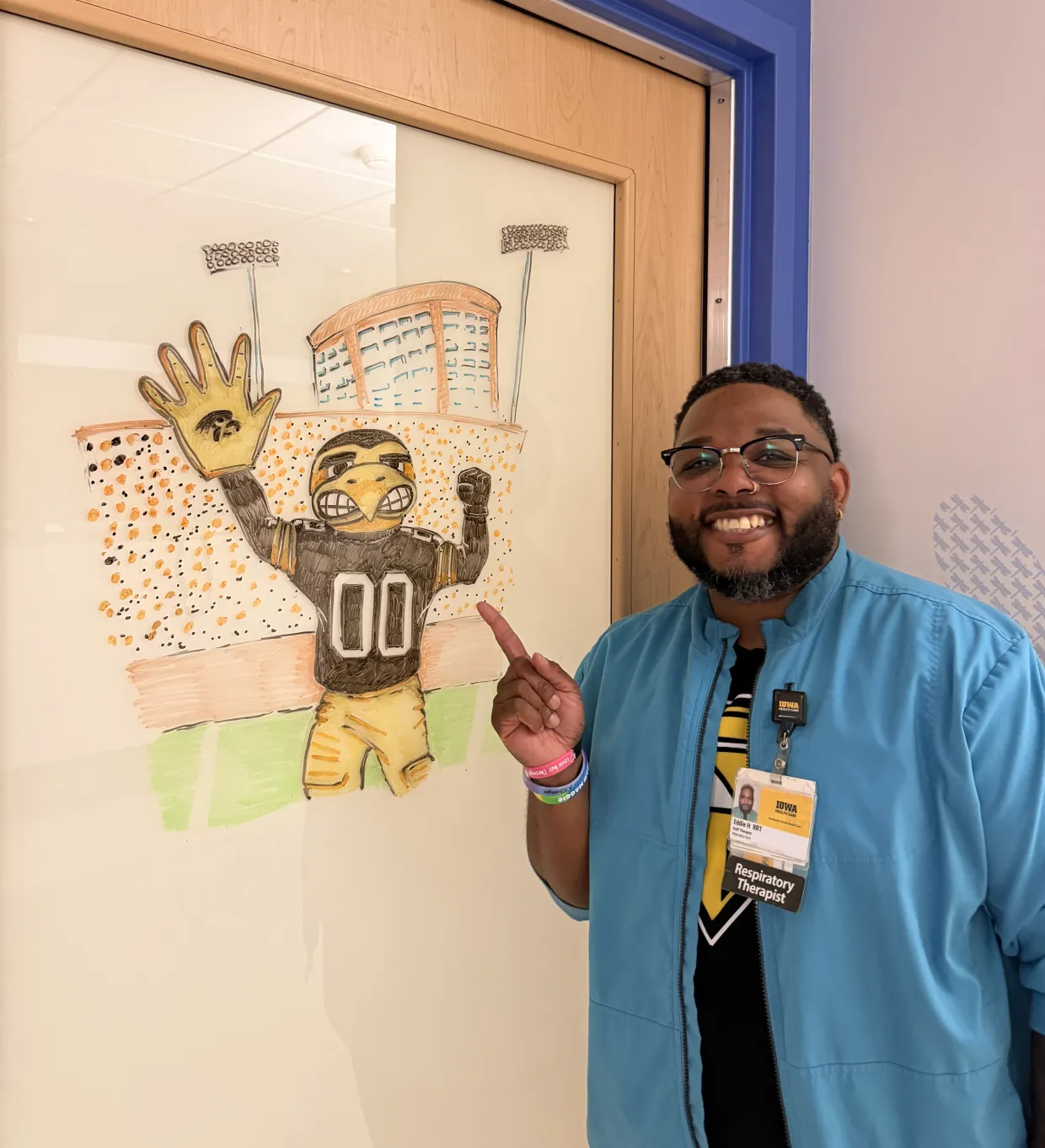 Respiratory therapist Eddie Hatcher poses with a Hawkeye-themed drawing created with dry erase markers on a patient room door. 