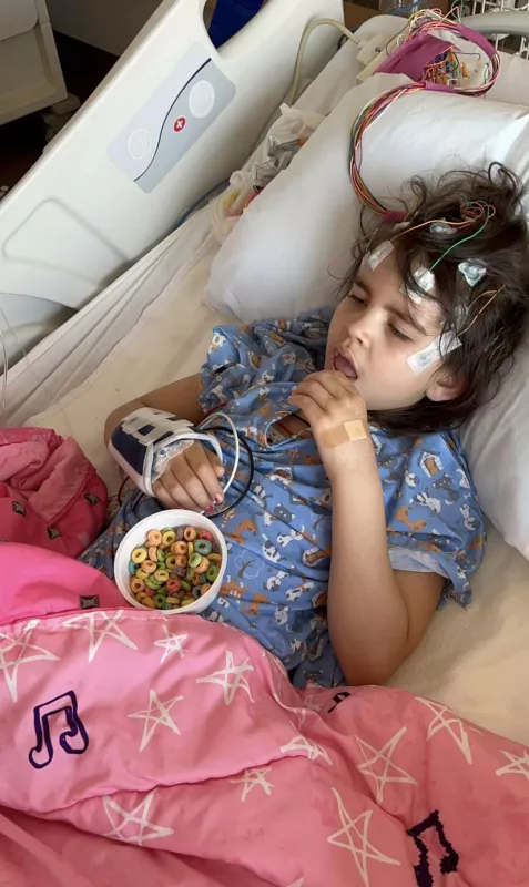 Eve Jimenez laying in hospital bed eating cereal