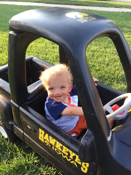 Young Nile Kron sitting in a play car with University of Iowa Hawkeye logo
