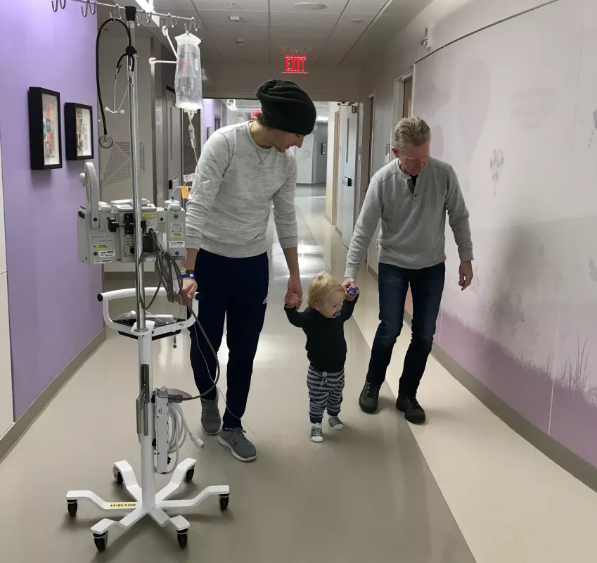 Atlas walking down a Stead Family Children’s Hospital hallway holding hands with his father and staff member