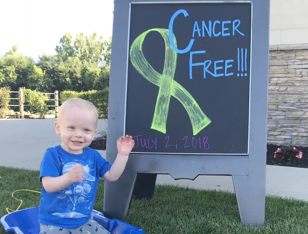 Kid Captain Atlas Coleman standing in front of  sign reading "Cancer Free"