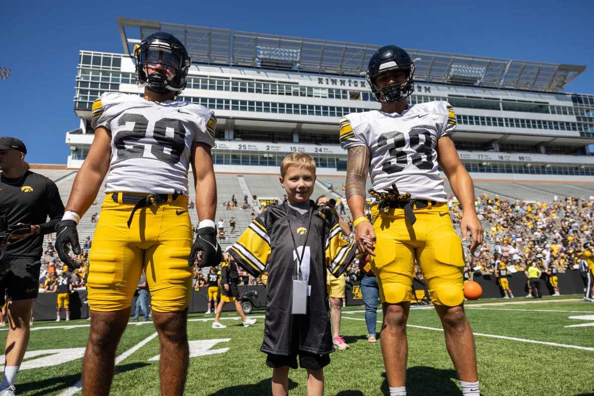 Kid Captain Aiden Washburn holding hand with two University of Iowa football players while attending Kid's Day 2024 at Kinnick Stadium