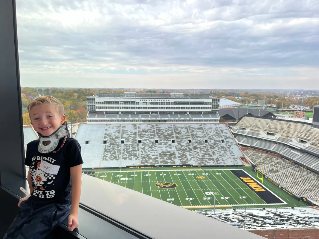 Kid Captain Luke Johnston standing in front of a window above Kinnick Stadium