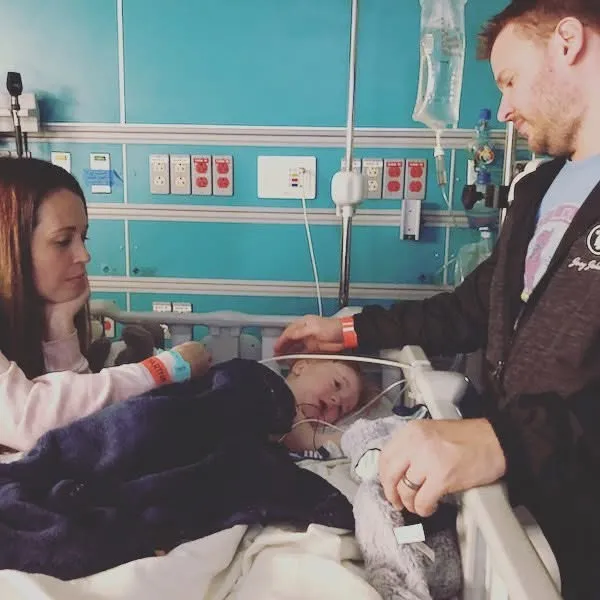 Kid Captain Luke Johnston laying in a hospital bed surrounded by his parents