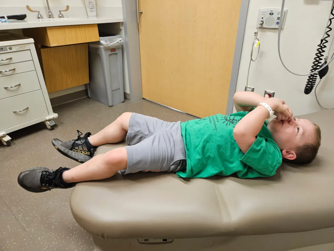 Kid Captain Micah Norby in a hospital exam room lying on a exam table