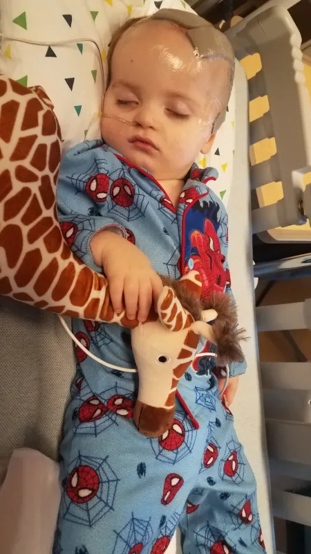 Kid captain Ray Walker asleep in a bed holding a stuffed giraffe