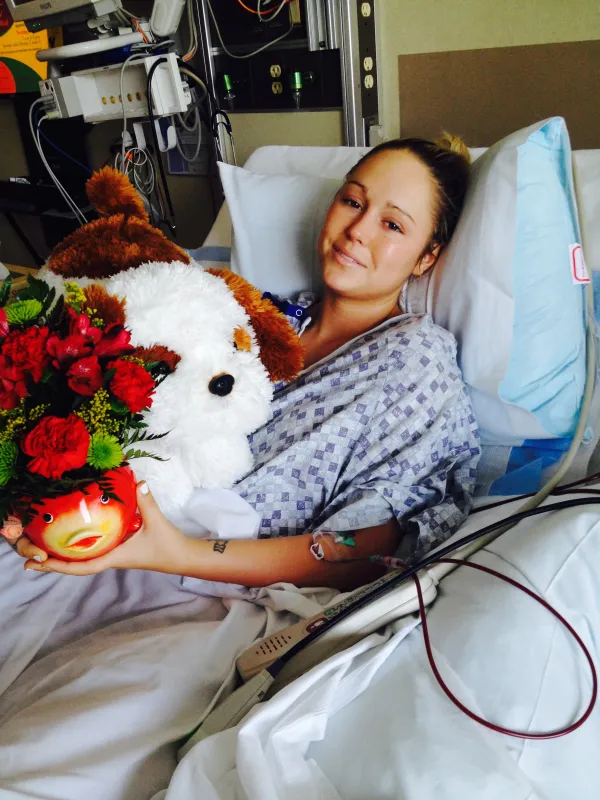 Bailey Cocklin in her hospital bed holding flowers and a dog stuffed animal.