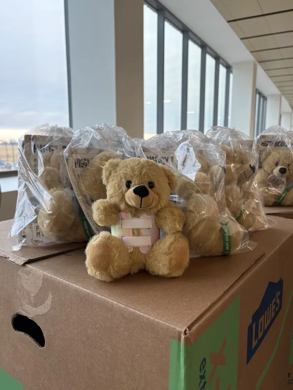 A custom teddy bear, donated by Meredith Secymore and Addy Blade, sitting on top of a box of packaged teddy bears.