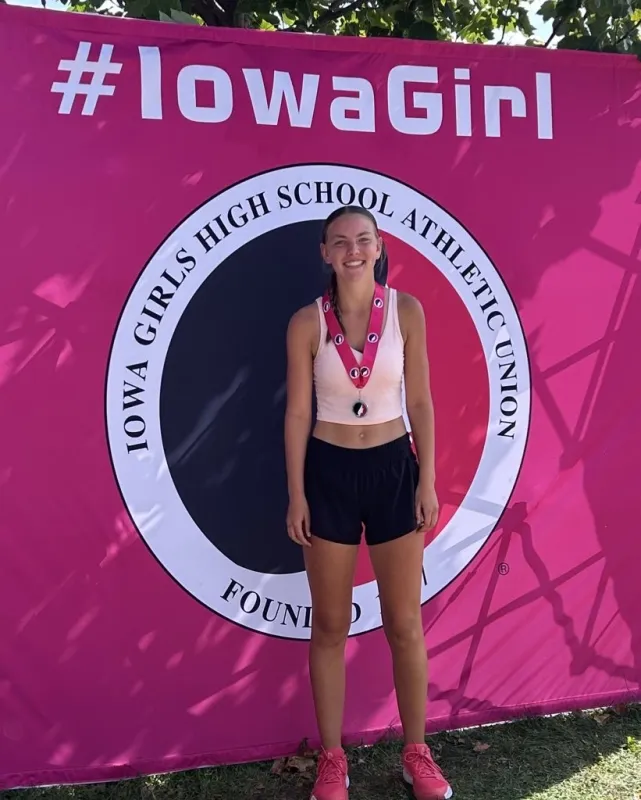 Mackenzie Sagers standing in front of a Iowa High School Tennis banner