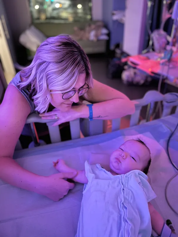 Bodhi laying in a hospital bed while holding his mother's hand.