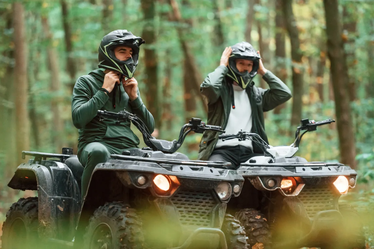 Two men riding an ATV while wearing helmets.