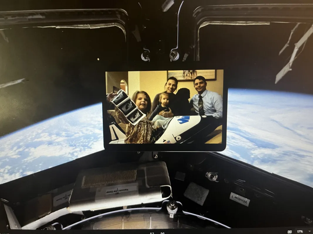 A photo of Dillyn Mumme and his family is displayed aboard the International Space Station, with Earth visible through the windows.
