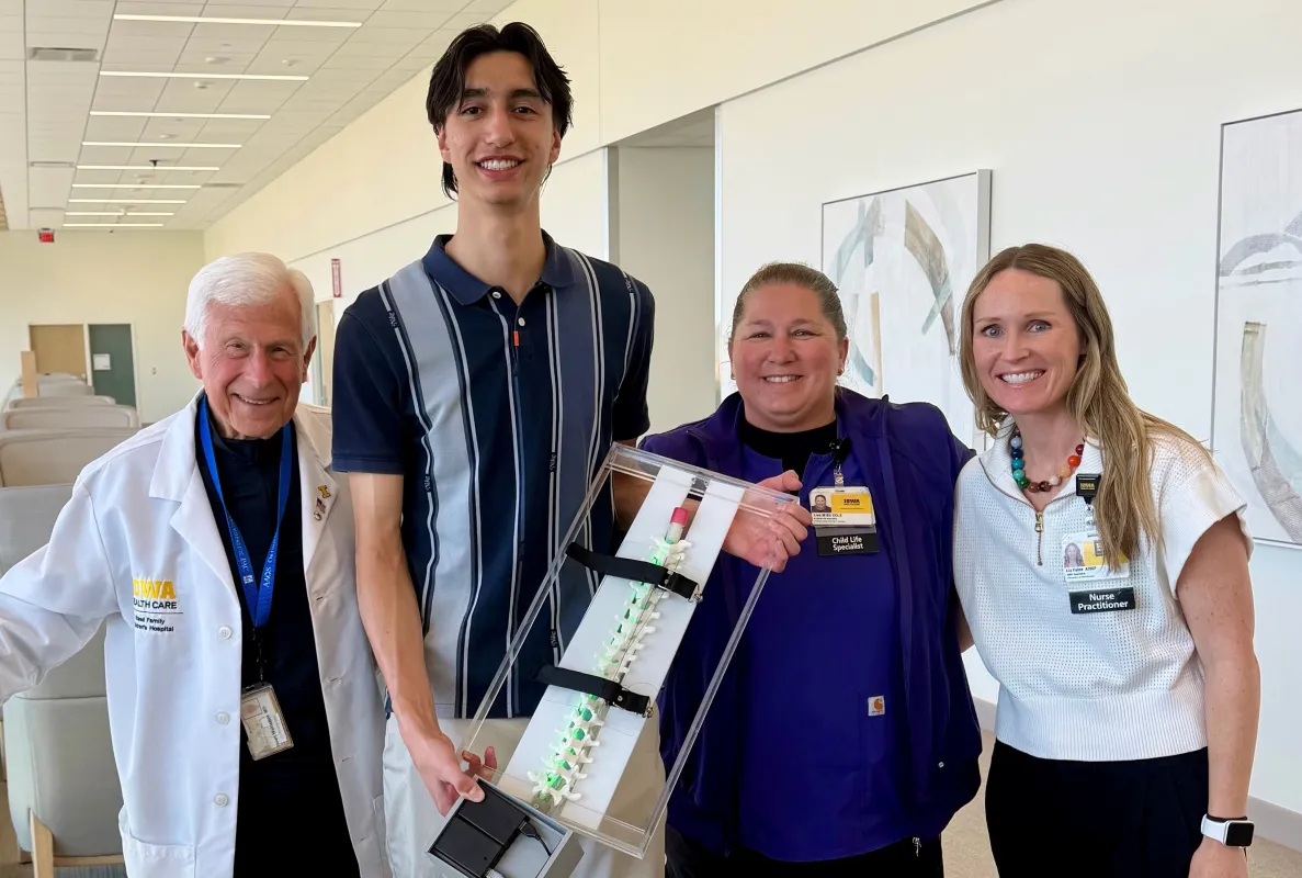 Collaboration played a key role in the creation of the spine model. Max Casini (holding the model) and his fellow students Aiden Dogic, Ronan Peach, and Grace Wohnoutka created the model in consultation with UI Health Care personnel, including Stuart Weinstein (left), Lisa Miguel (second from right), and Liz Faine. Weinstein is a pediatric surgeon, Miguel is a senior child life specialist, and Faine is a nurse practitioner.