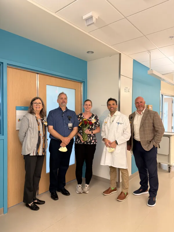 Laura Corbett, center, stands with Stead Family Children’s Hospital leaders outside Room 604, which was named in her honor in recognition of her work and impact in the NICU.