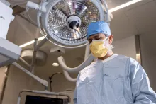 Paari Dominic wears full surgical scrubs standing in front of a light in a cardiac catheterization lab.