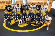 Kid Captains and members of the Iowa football team pause for a group photo inside the locker room at Kinnick Stadium.
