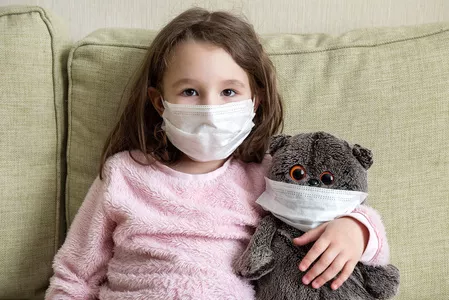 Child wearing mask with her teddy bear